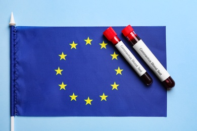 Photo of Test tubes with blood samples and European Union flag on light blue background, flat lay. Coronavirus outbreak
