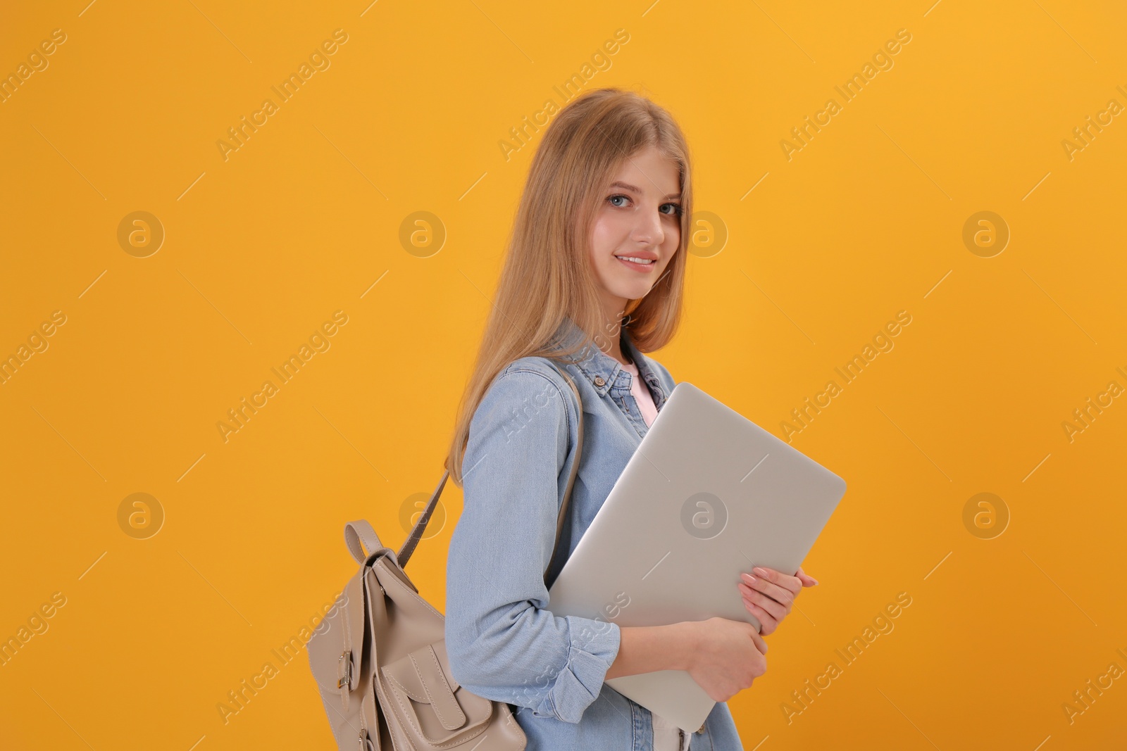 Photo of Teenage student with laptop and backpack on yellow background