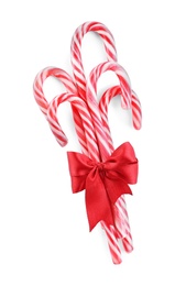 Photo of Sweet Christmas candy canes with red bow on white background, top view