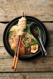 Photo of Delicious ramen with chopsticks and spoon in bowl on wooden table, top view. Noodle soup