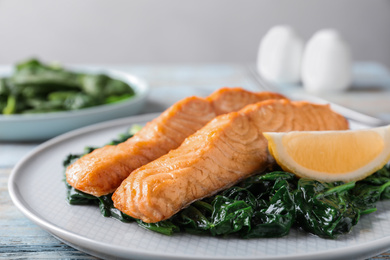 Photo of Tasty salmon with spinach and lemon on wooden table, closeup