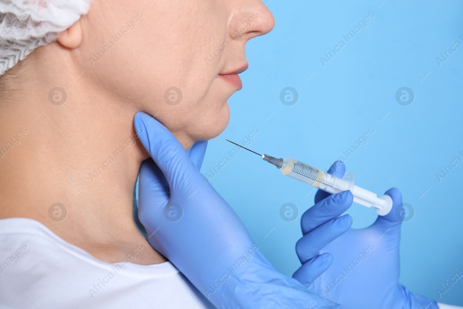 Photo of Mature woman with double chin receiving injection on blue background, closeup