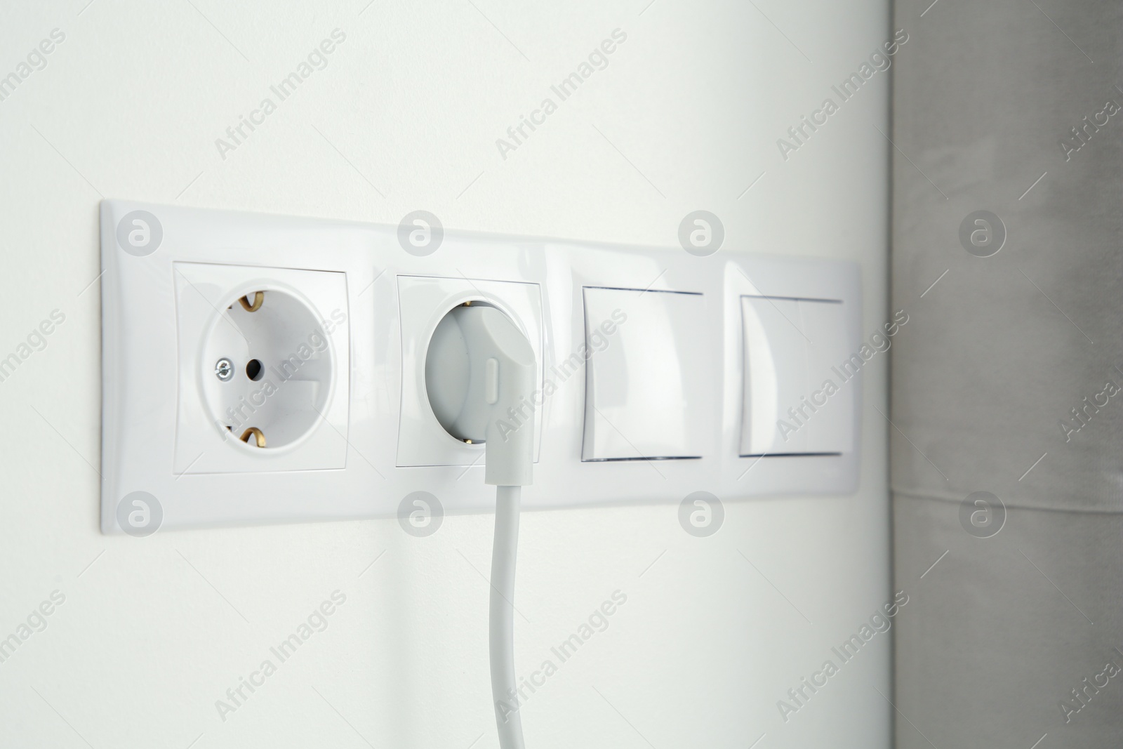 Photo of Power sockets with inserted plug and light switches on white wall indoors