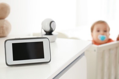 Photo of Baby monitor and camera on chest of drawers near crib with child in room. Video nanny