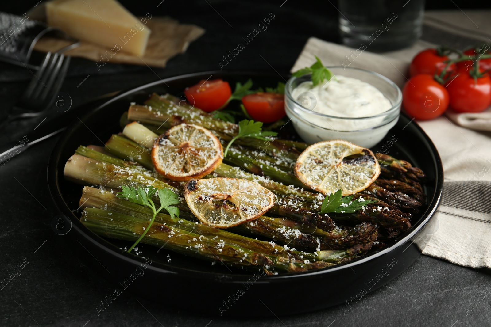 Photo of Oven baked asparagus with lemon slices served on black table, closeup