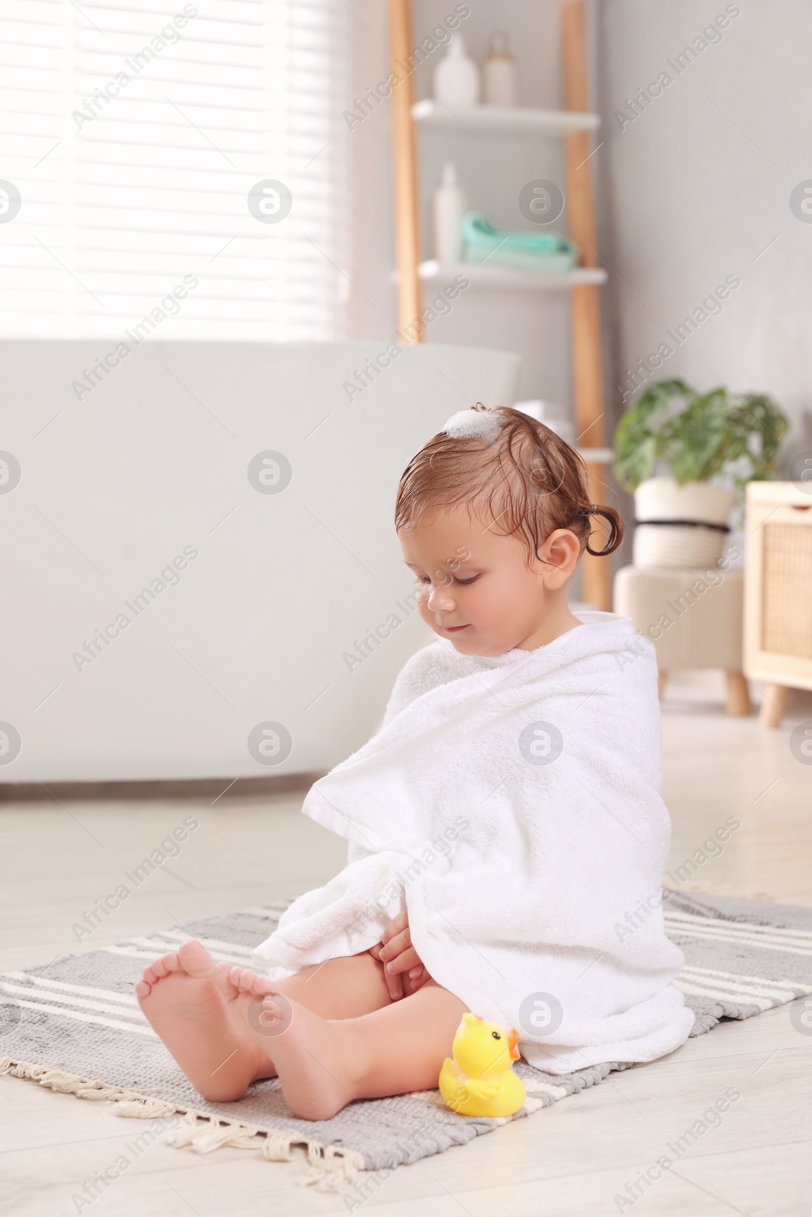 Photo of Cute little girl wrapped with towel after bath in room