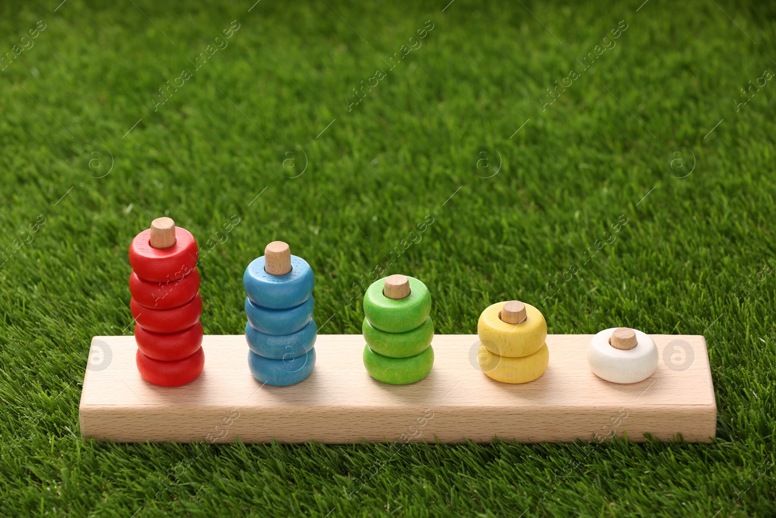 Photo of Stacking and counting game wooden pieces on artificial grass, space for text. Educational toy for motor skills development