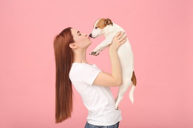 Woman kissing her cute Jack Russell Terrier dog on pink background