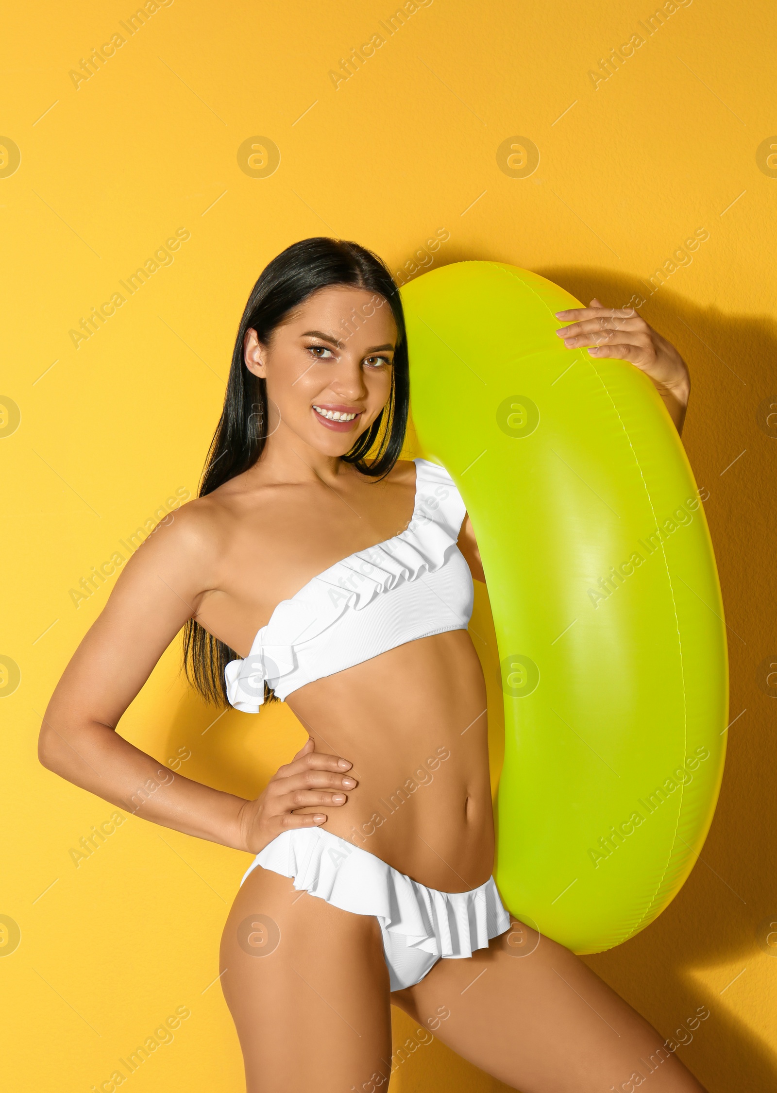 Photo of Beautiful young woman in white bikini with inflatable ring on yellow background