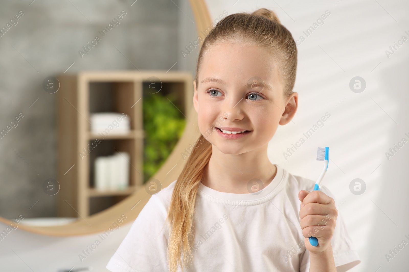 Photo of Cute little girl holding plastic toothbrush in bathroom, space for text