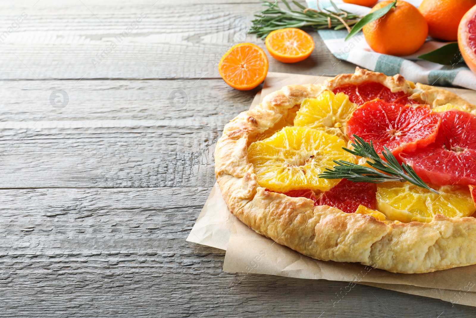 Photo of Delicious galette with citrus fruits and rosemary on wooden table. Space for text