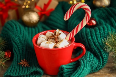 Photo of Cup of tasty cocoa with marshmallows and Christmas candy cane on wooden table