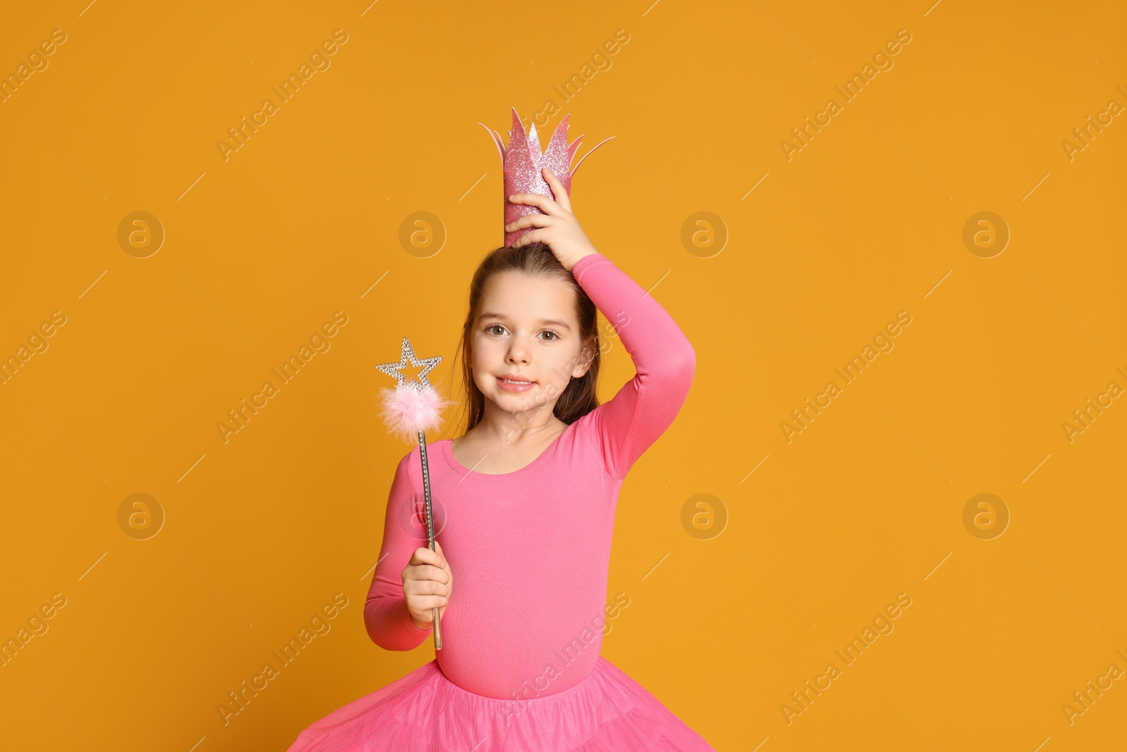 Photo of Cute girl in pink crown with magic wand on yellow background, space for text. Little princess
