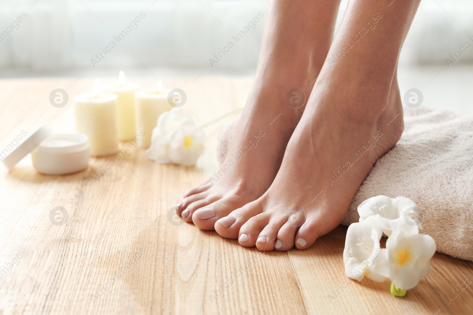 Photo of Woman with beautiful feet, towel and flowers on wooden floor, closeup. Spa treatment