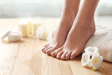 Woman with beautiful feet, towel and flowers on wooden floor, closeup. Spa treatment