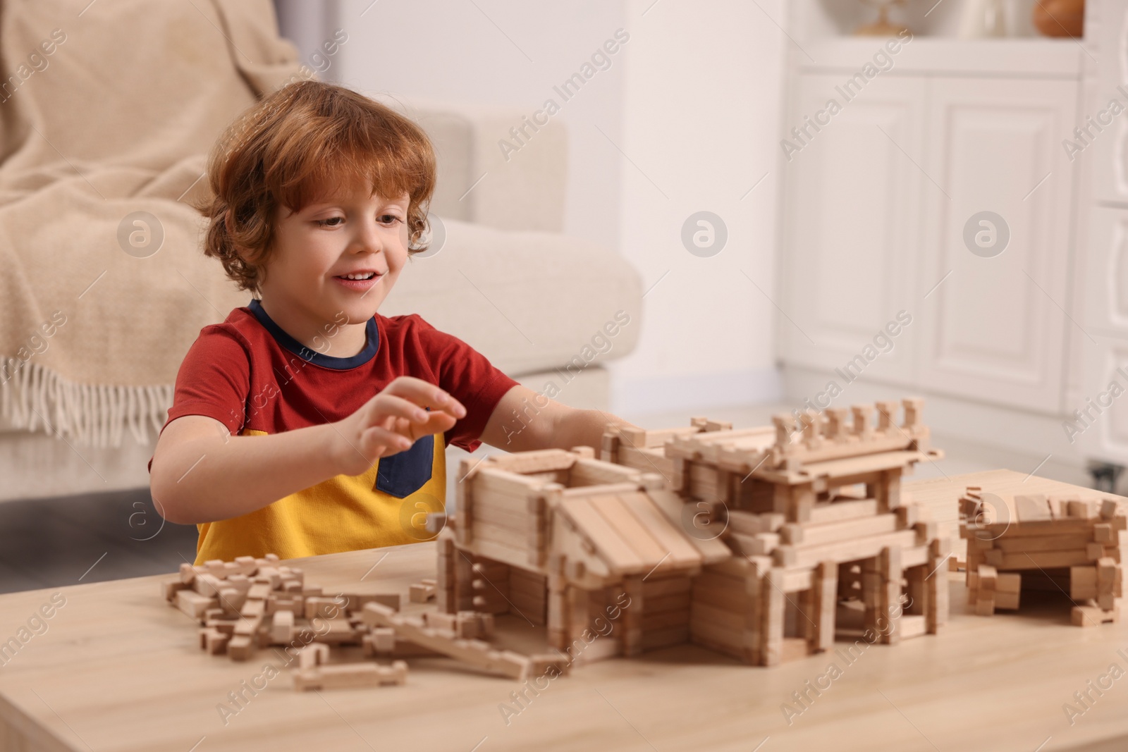 Photo of Cute little boy playing with wooden construction set at table in room. Child's toy