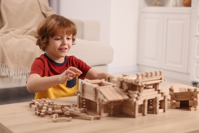 Photo of Cute little boy playing with wooden construction set at table in room. Child's toy