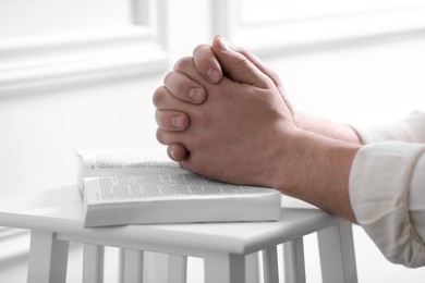 Religion. Christian man praying over Bible indoors, closeup