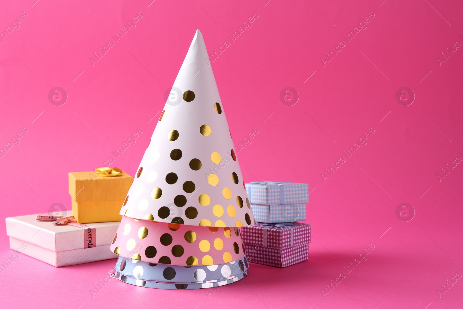 Photo of Party hats and gift boxes on pink background, space for text