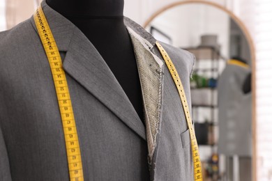 Photo of Mannequin with unfinished jacket and measuring tape in tailor shop, closeup