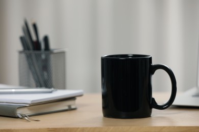 Photo of Black ceramic mug and notebooks on wooden table at workplace. Space for text