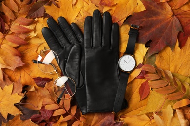 Photo of Stylish black leather gloves, glasses and wristwatch on dry leaves, flat lay