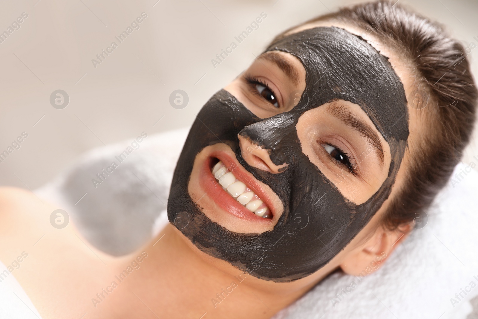 Photo of Beautiful woman with black mask on face relaxing in spa salon, closeup