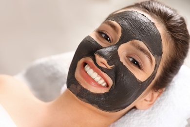 Beautiful woman with black mask on face relaxing in spa salon, closeup