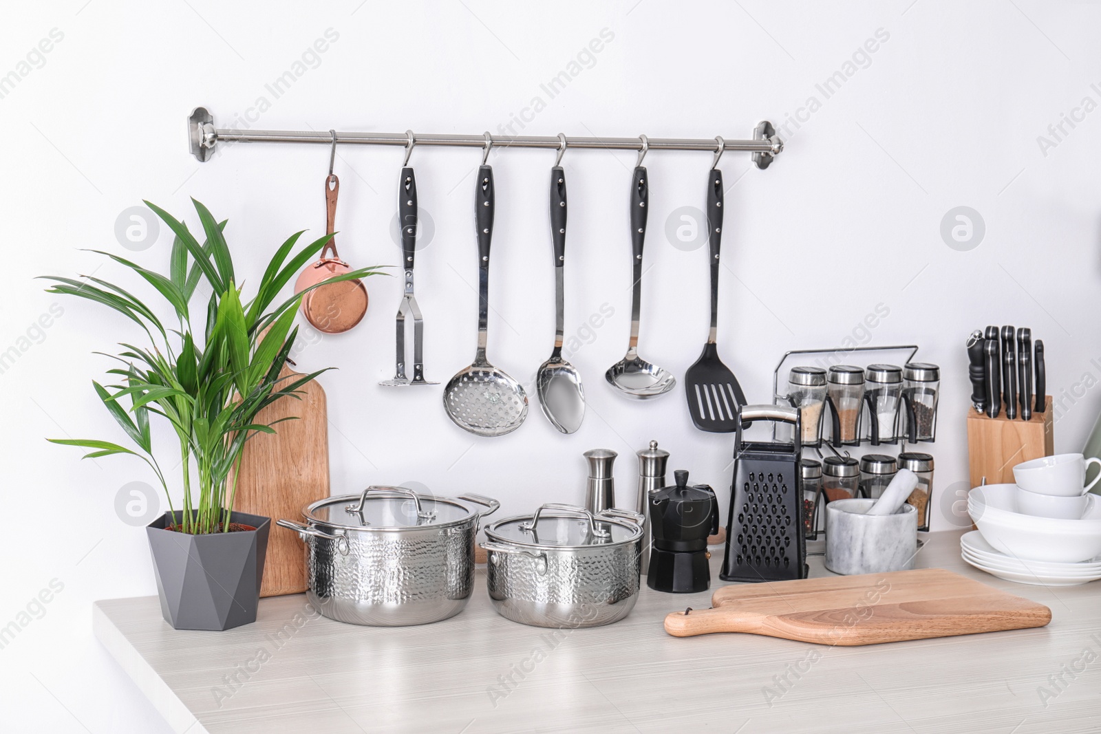 Photo of Set of clean cookware, dishes, utensils and appliance on table at white wall