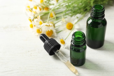 Chamomile flowers and cosmetic bottles of essential oil on wooden table, closeup. Space for text