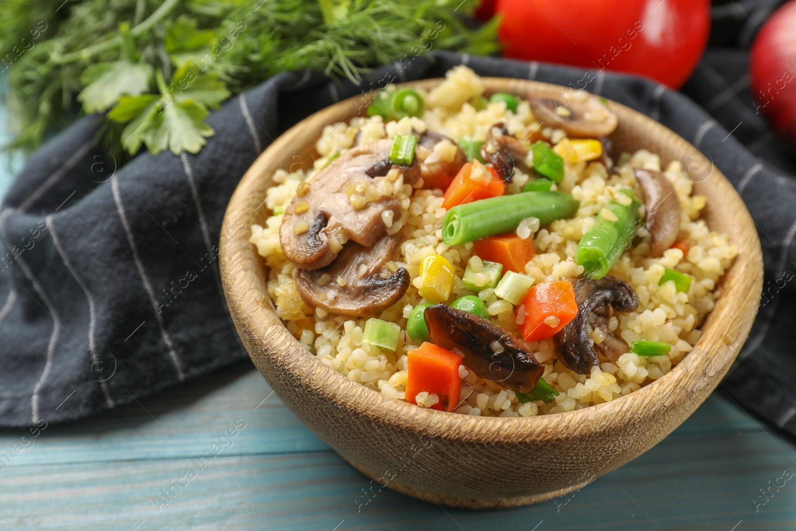 Photo of Delicious bulgur with vegetables and mushrooms on light blue wooden table, closeup