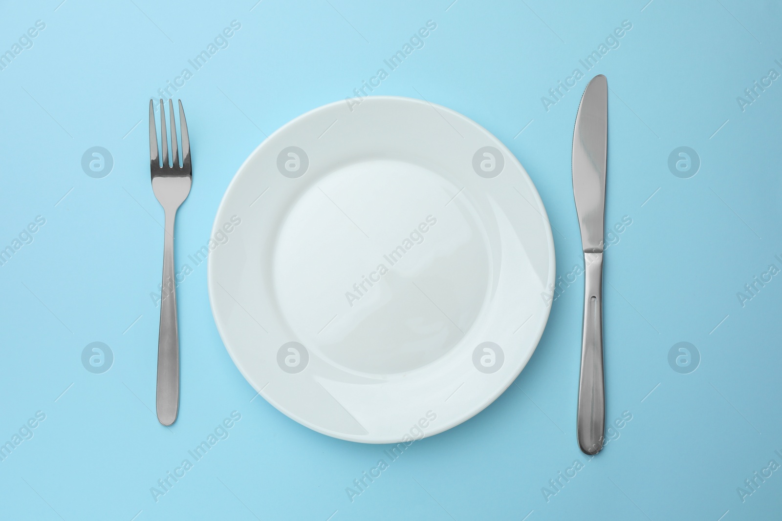 Photo of Clean plate, fork and knife on light blue background, top view