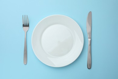 Clean plate, fork and knife on light blue background, top view