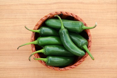 Photo of Bowl of fresh green jalapeno peppers on wooden table, top view
