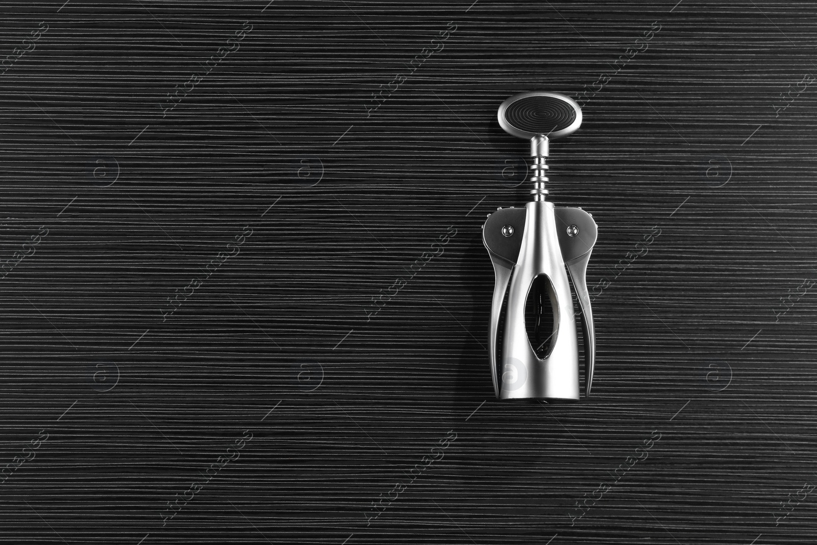Photo of One wing corkscrew on black wooden table, top view. Space for text