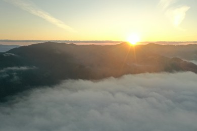 Photo of Aerial view of beautiful mountains covered with fluffy clouds at sunrise