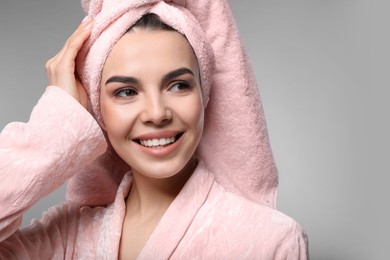 Happy young woman in bathrobe with towel on head against light grey background. Washing hair