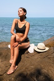 Beautiful young woman in stylish bikini sitting on rock near sea