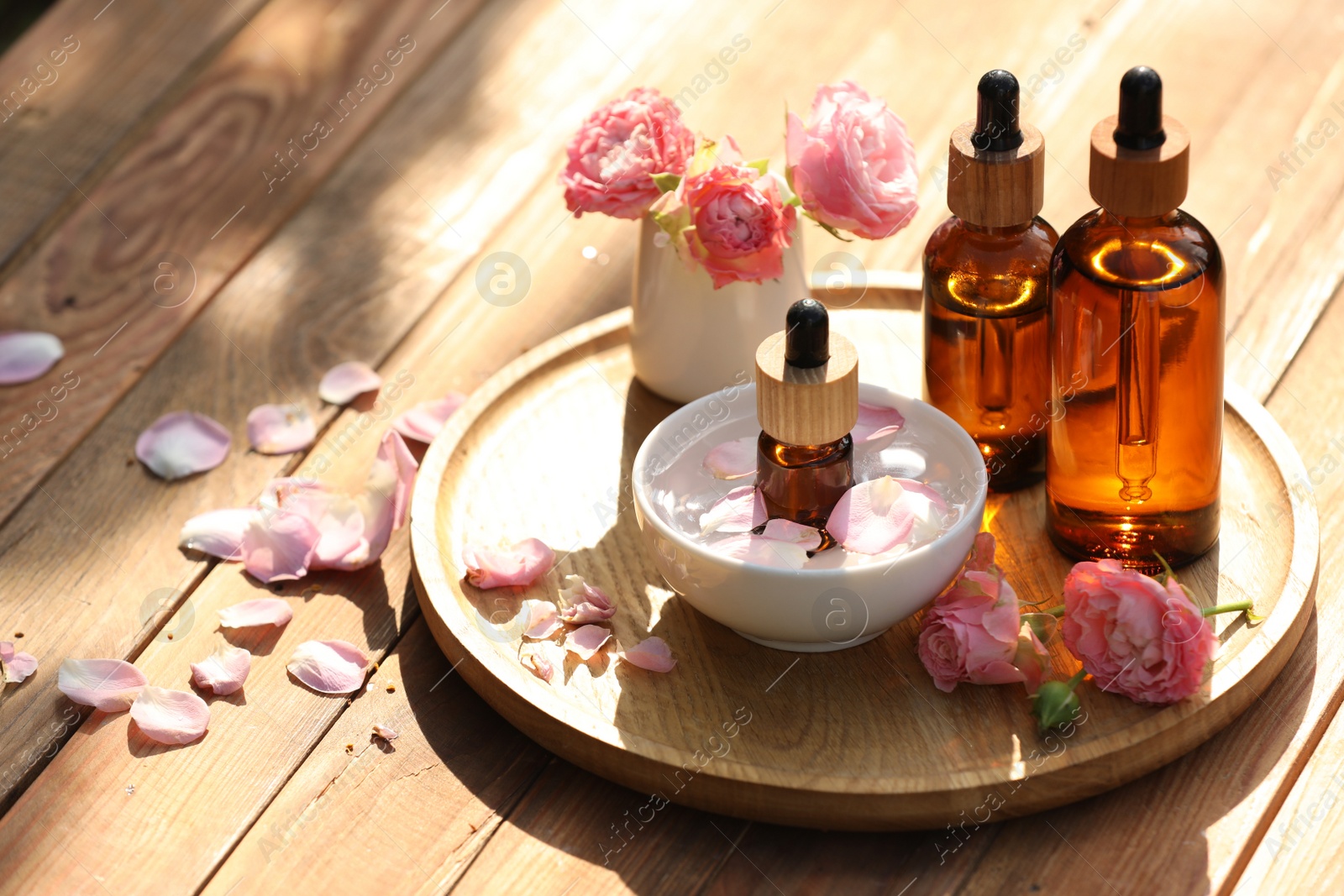 Photo of Bottles of rose essential oil and flowers on wooden table, space for text