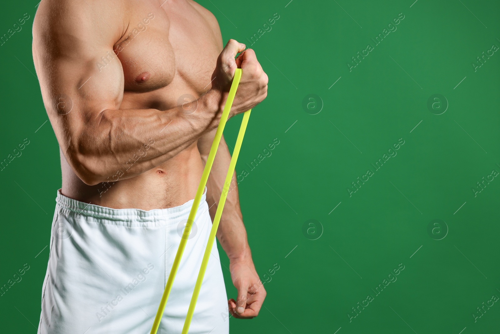 Photo of Muscular man exercising with elastic resistance band on green background, closeup. Space for text