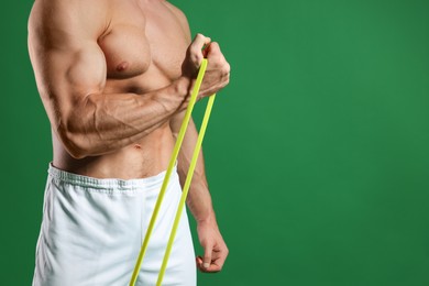 Photo of Muscular man exercising with elastic resistance band on green background, closeup. Space for text