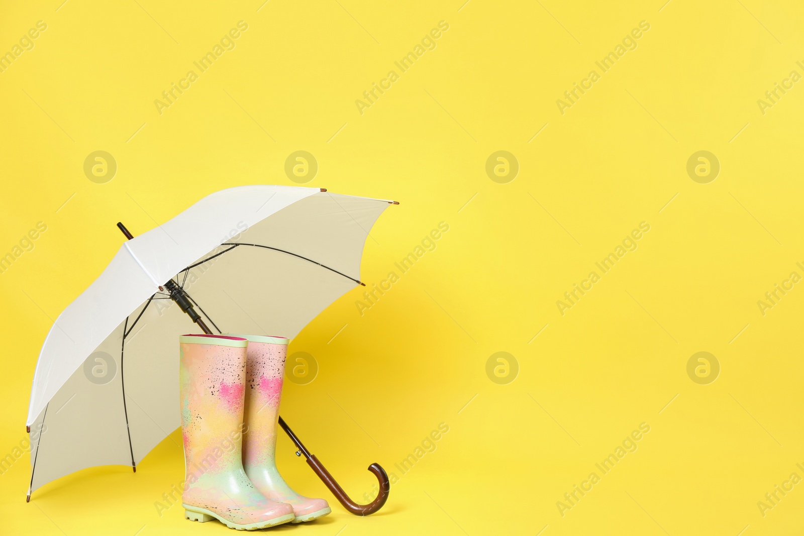 Photo of Beautiful white umbrella and colorful rubber boots on light yellow background. Space for text