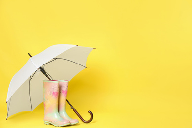 Beautiful white umbrella and colorful rubber boots on light yellow background. Space for text