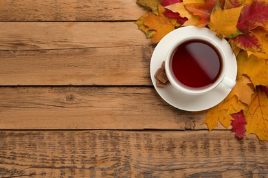 Cup of hot tea and autumn leaves on wooden table, flat lay. Space for text