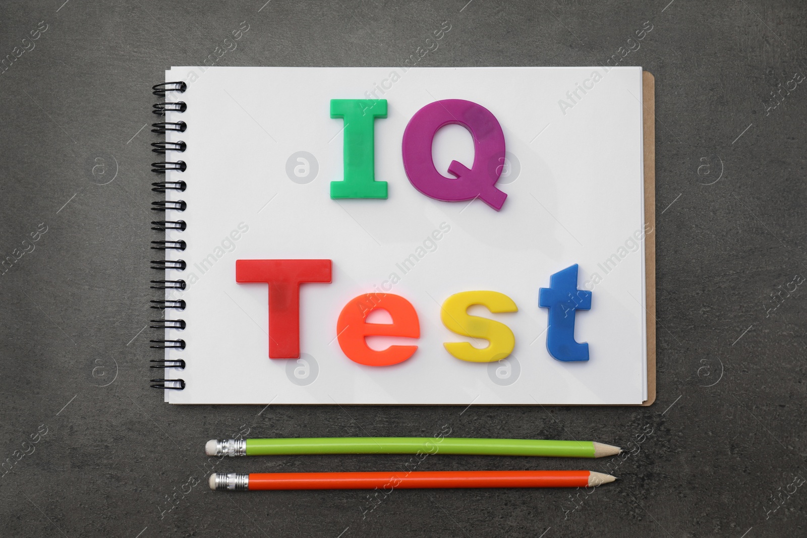 Photo of Notebook with words IQ Test made of magnets and pencils on black table, flat lay