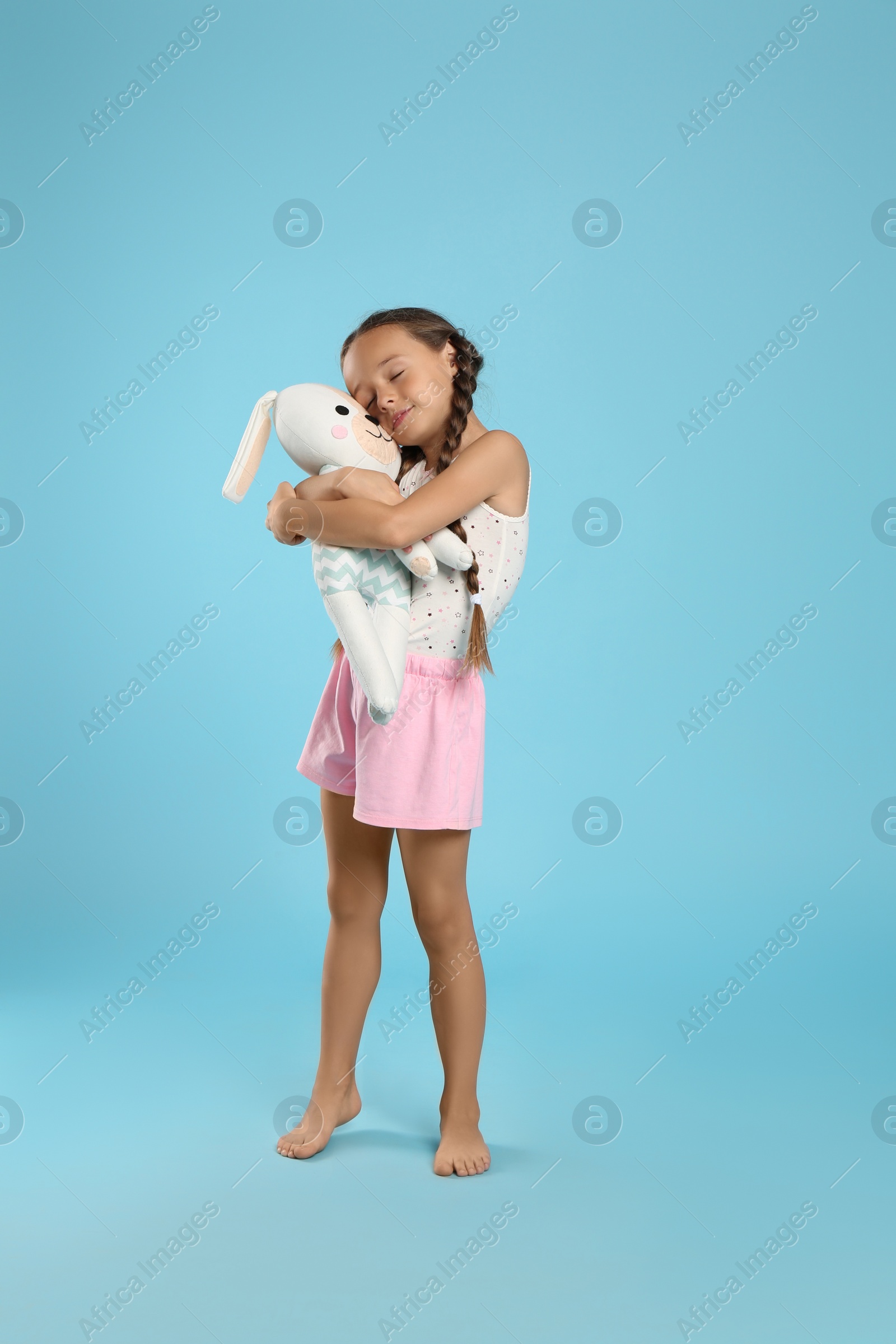 Photo of Cute girl wearing pajamas with toy on light blue background