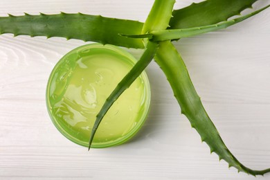 Jar of cosmetic gel and aloe vera leaves on white wooden table, top view