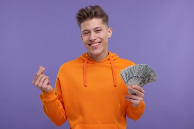 Photo of Happy man with dollar banknotes showing money gesture on purple background