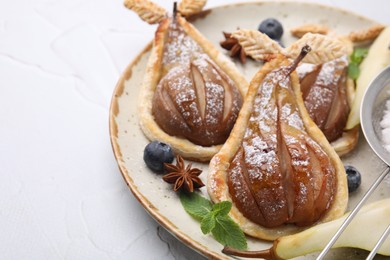 Delicious pears baked in puff pastry with powdered sugar served on white table, closeup. Space for text
