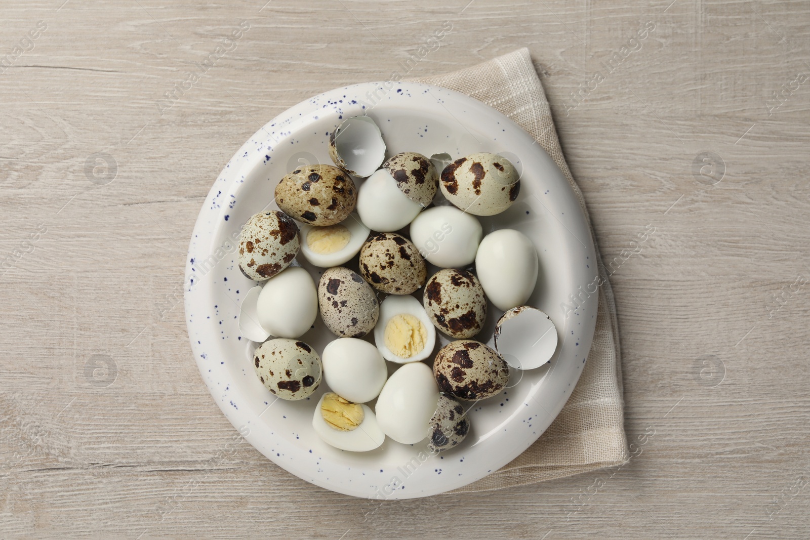 Photo of Unpeeled and peeled hard boiled quail eggs in bowl on white wooden table, top view